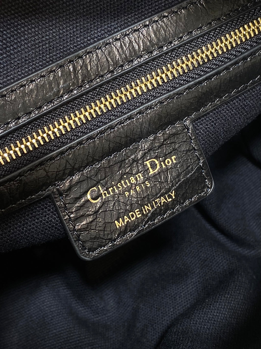Black Dior leather bag with gold zipper and 'Made in Italy' logo patch