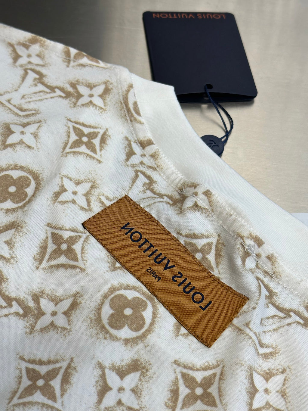 Cream T-shirt with gold monogram fabric and brown Louis Vuitton label tag.