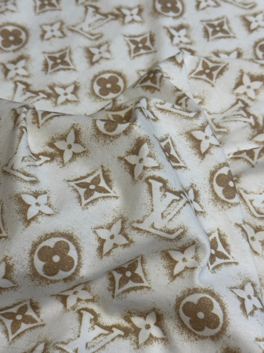 Cream T-shirt fabric with repeating gold monogram pattern.