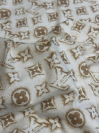 Cream T-shirt fabric with repeating gold monogram pattern.