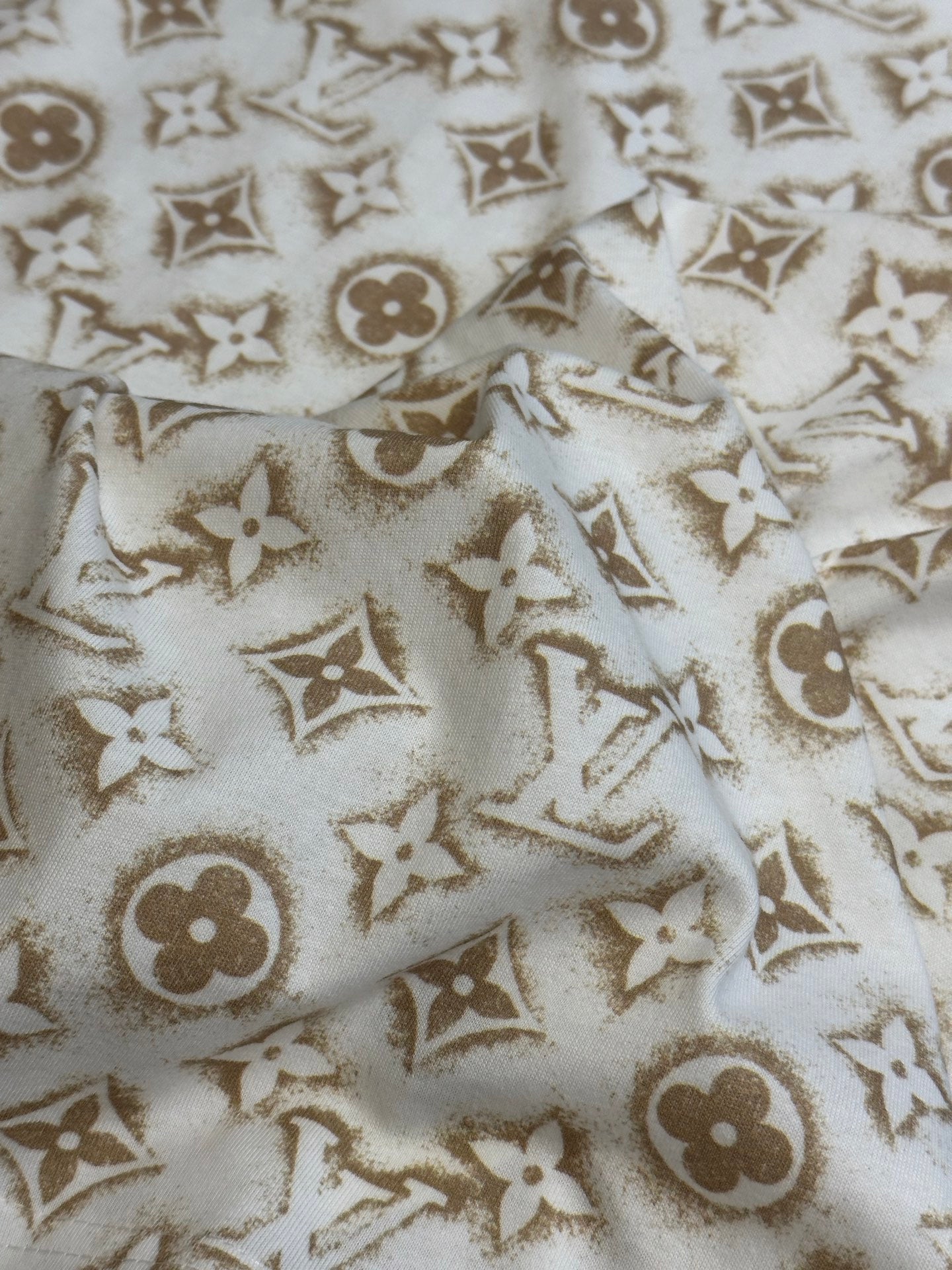 Cream T-shirt fabric with repeating gold monogram pattern.