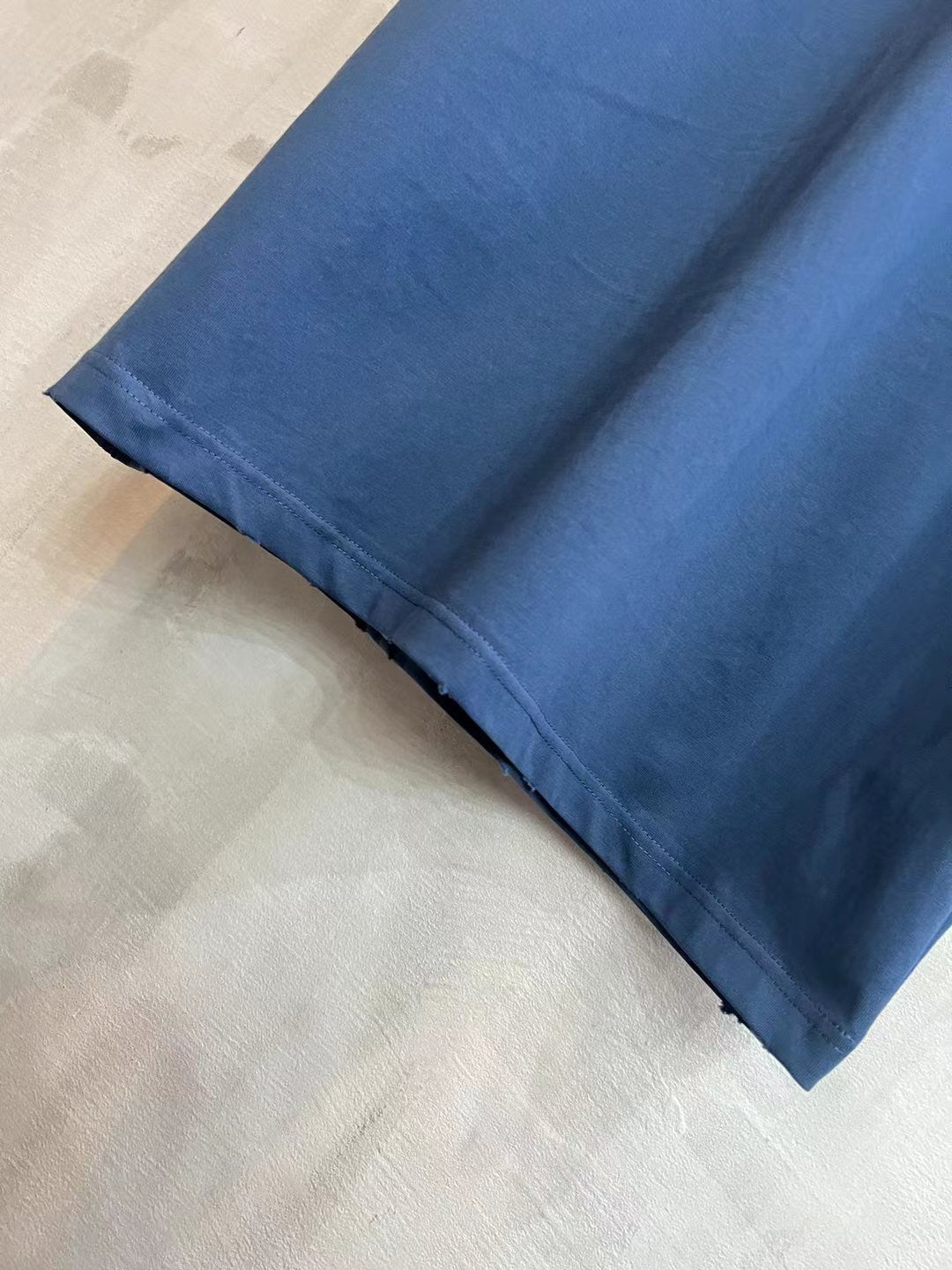 Blue T-shirt fabric and side hem close-up with drape and sleeve edge.
