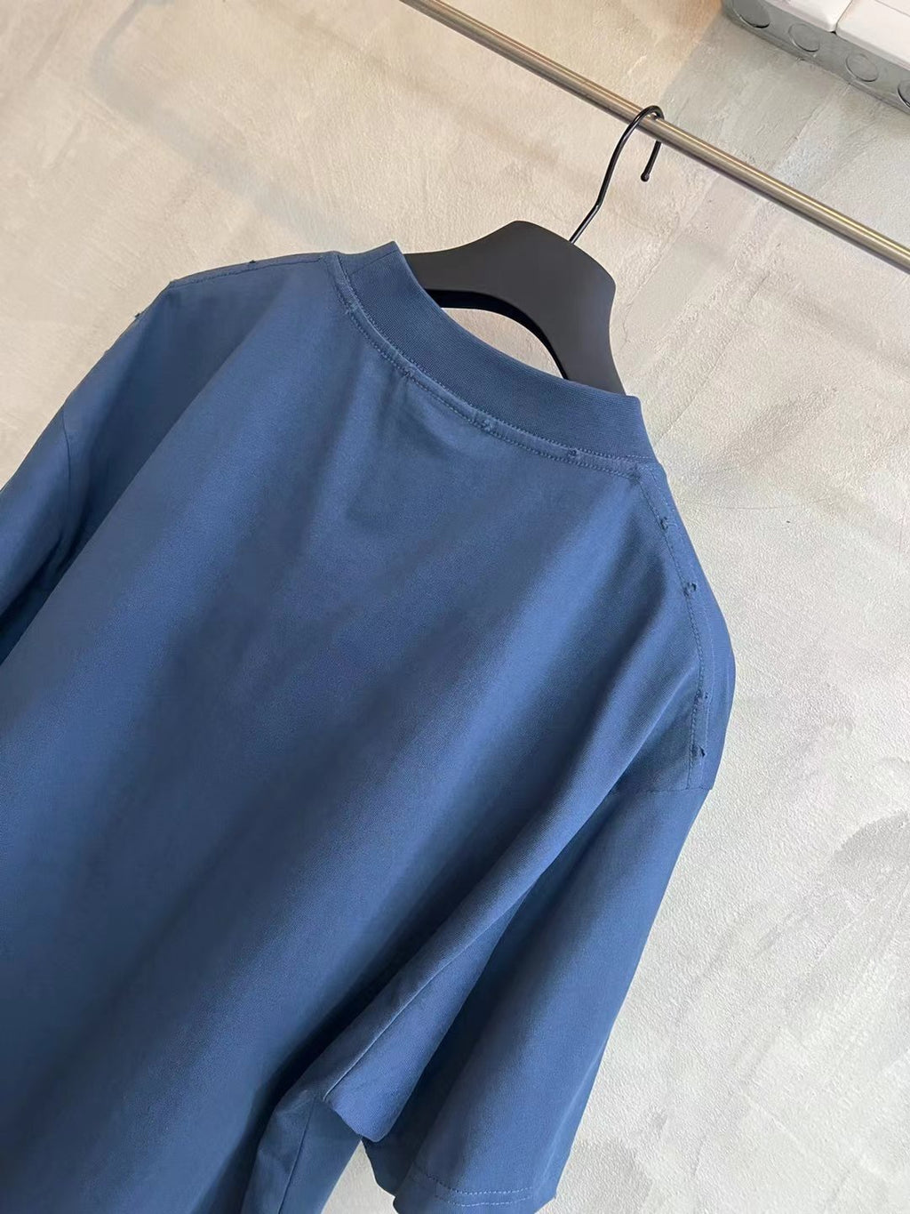 Blue T-shirt upper back and shoulder seam close-up on hanger.