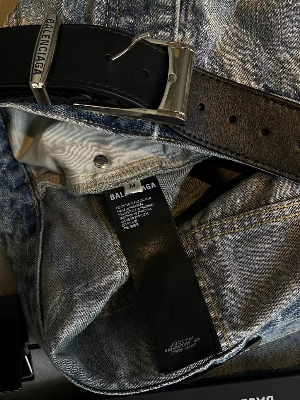 Light blue denim pants with black belt, metal buckle, and BALENCIAGA hang tag
