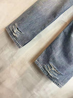 Light blue denim pants laid flat, showing knee rips and frayed hems