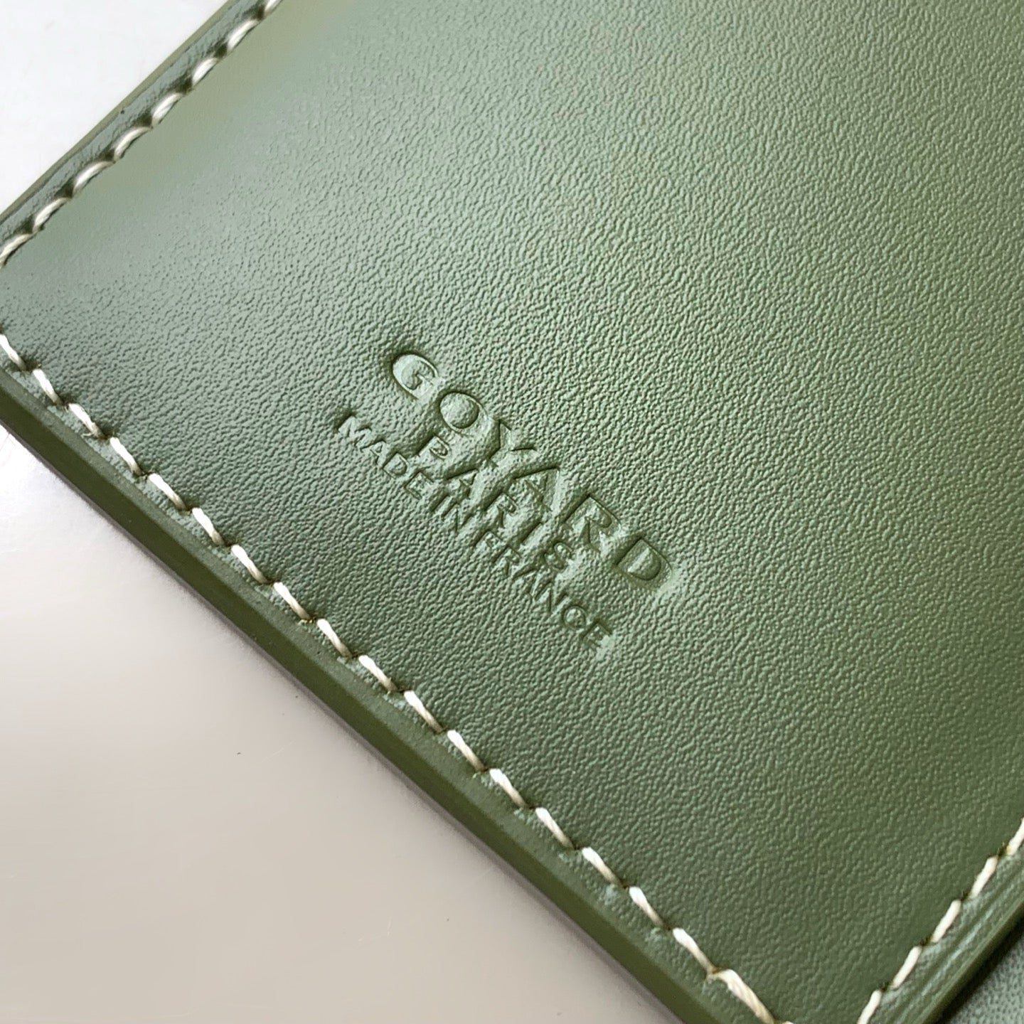 Embossed text on green leather card holder with white-stitched edge