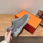 Gray suede lace-up sneaker on orange box, ridged sole with bold geometric tread