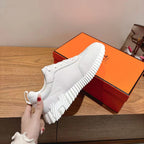 Hermes unisex white sneaker held up by hand; textured white sole and laces