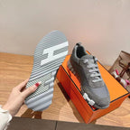 Gray suede sneaker outsole view, textured tread with logo-style stripes, on box