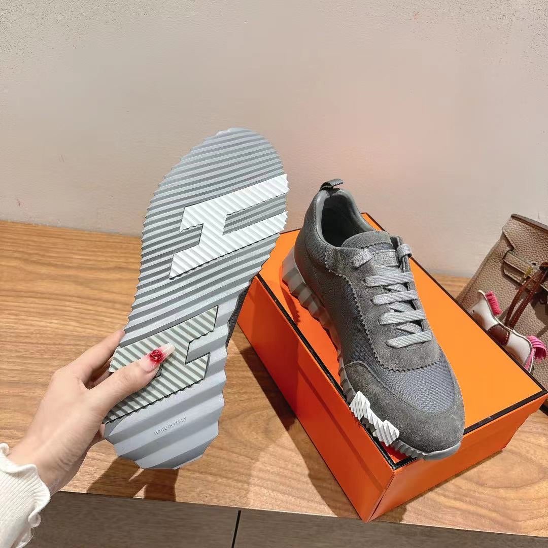 Gray suede sneaker outsole view, textured tread with logo-style stripes, on box