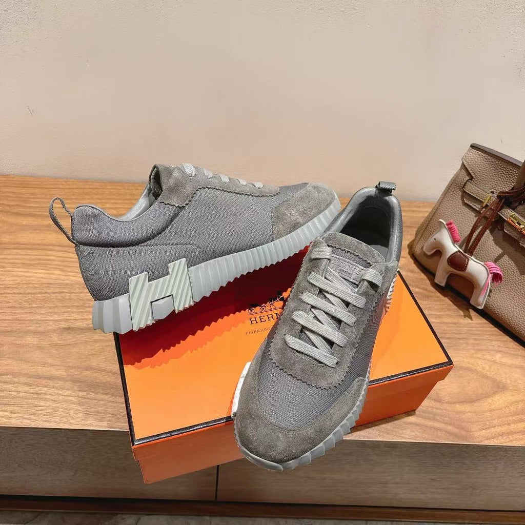 Gray suede lace-up sneakers with bold striped sole detail, on orange shoebox