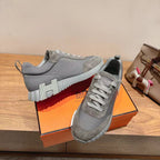 Gray suede lace-up sneakers with bold striped sole detail, on orange shoebox