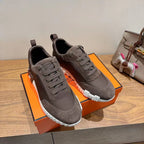 Grey suede sneakers, two-lace pairs on display with white ribbed soles, Hermes