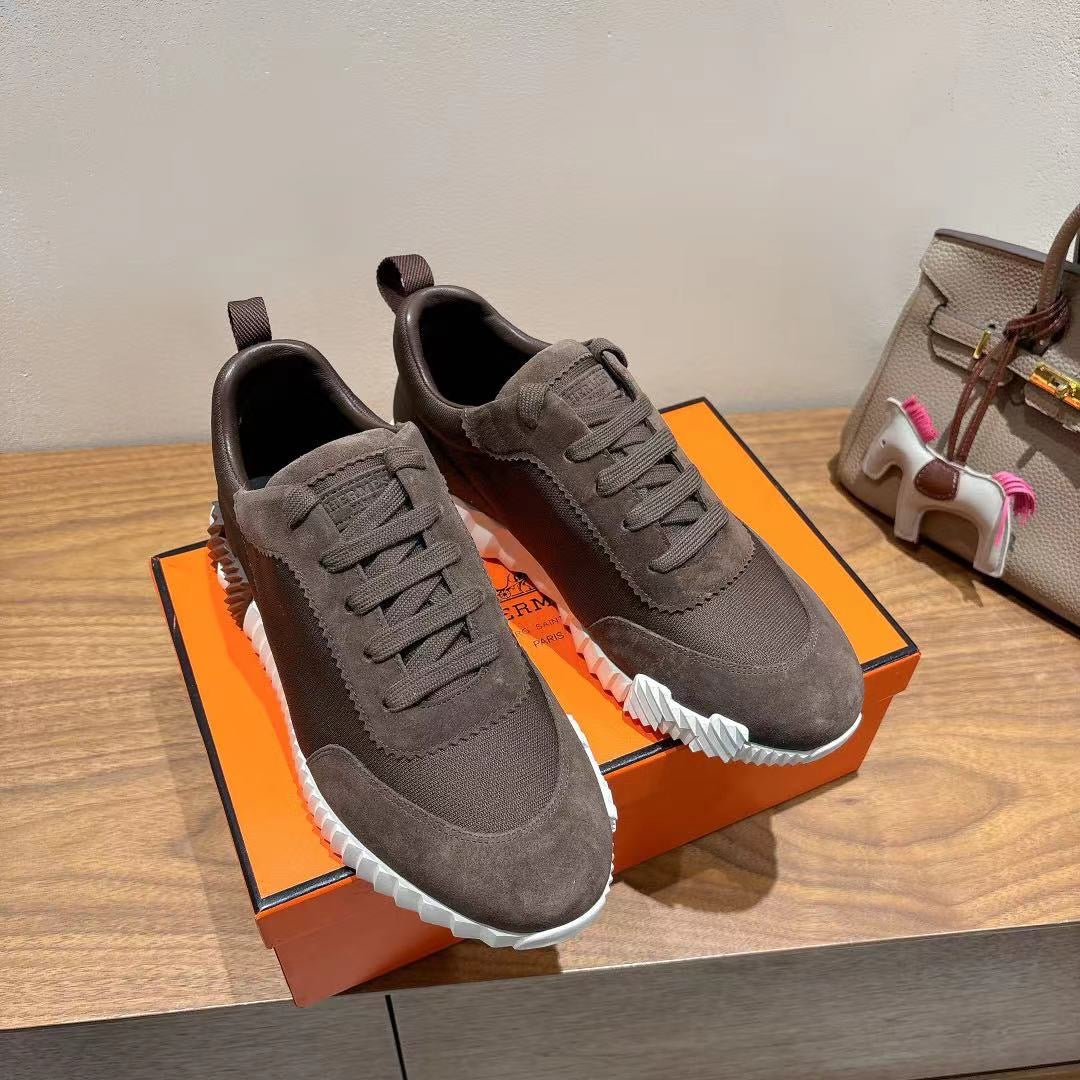 Grey suede sneakers, two-lace pairs on display with white ribbed soles, Hermes