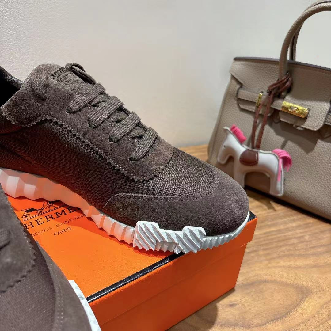 Grey suede lace-up sneakers close-up, white ribbed sole and stitched panel, Hermes