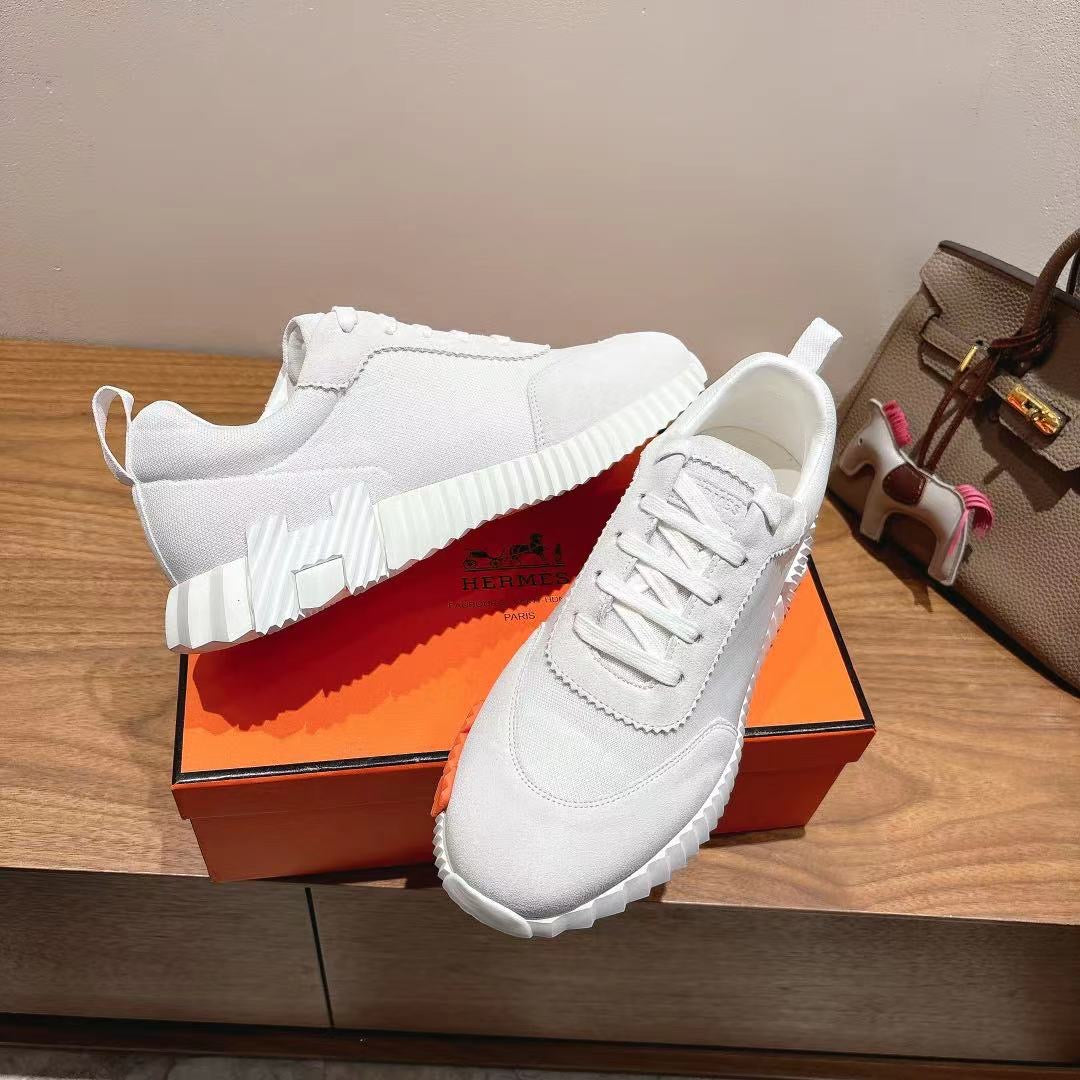 Hermes unisex white sneakers with orange outsole accents on display