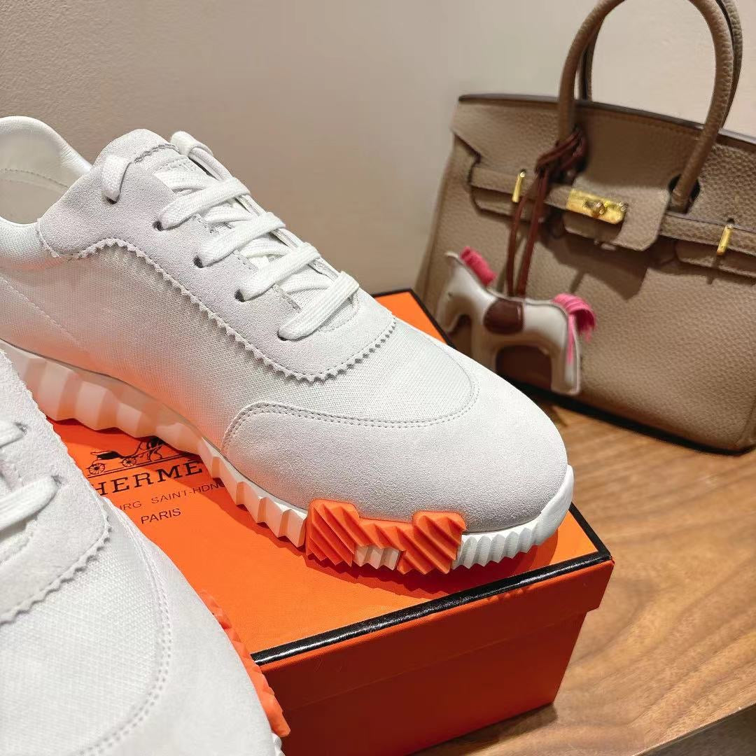 Hermes unisex white sneakers close-up with orange outsole and lace-up panels