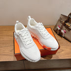 Hermes unisex white sneakers on orange box; lace-up design and orange sole