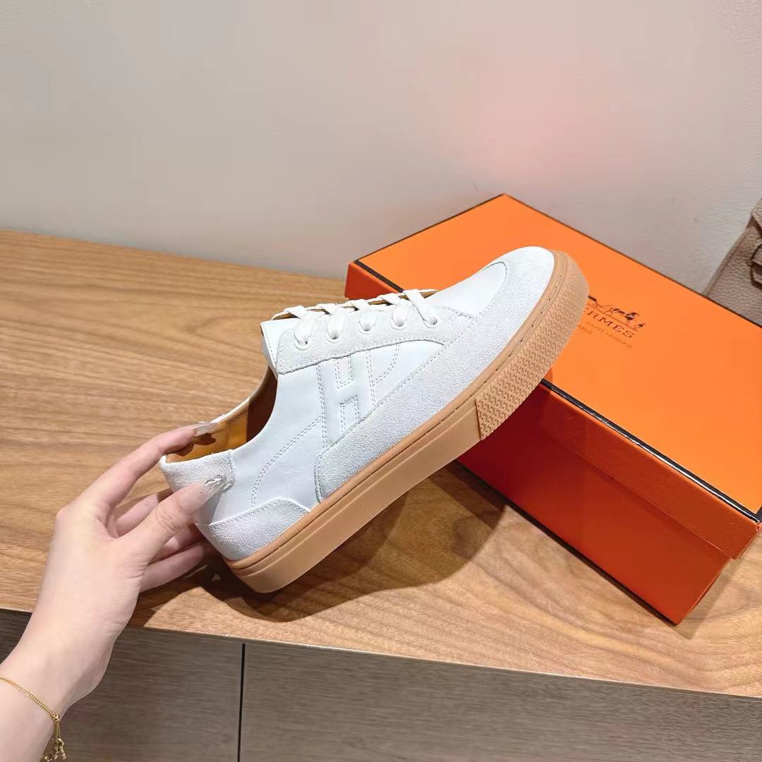 White leather lace-up sneaker held in hand, tan rubber sole