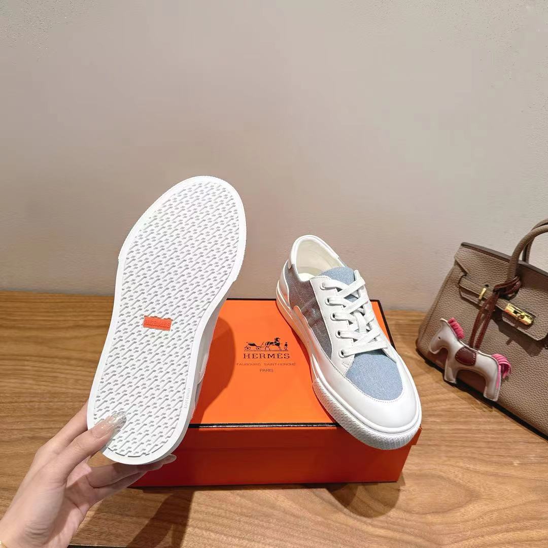 White and light-blue sneakers outsole view with red brand mark on tread.