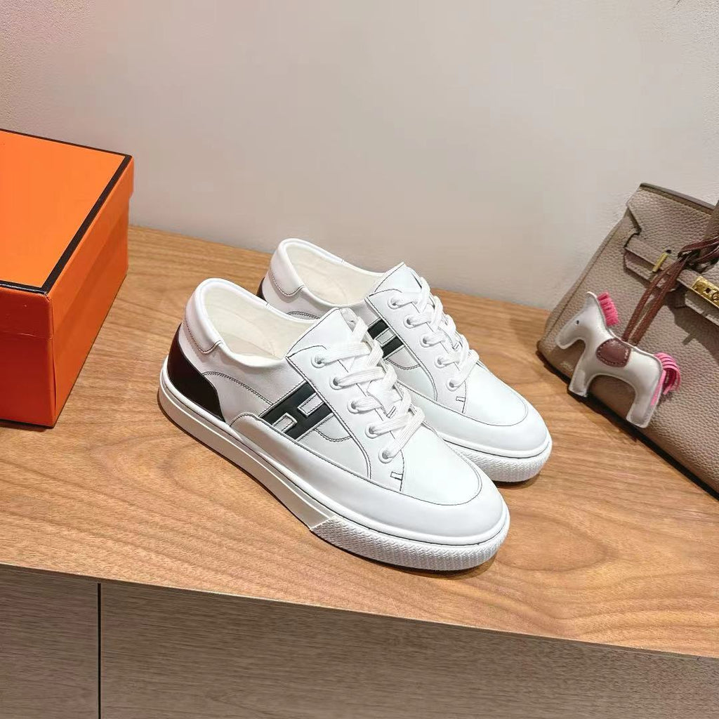 White Hermes unisex luxury sneakers with black side logo panel, on orange box.