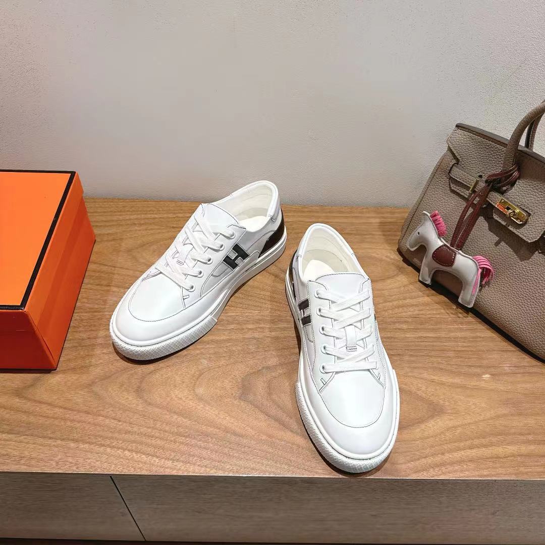 White Hermes unisex luxury sneakers, side view with black logo and white laces.