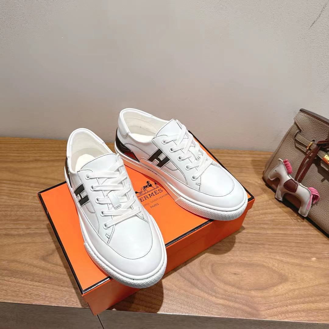 White Hermes unisex sneakers with black side stripe, lace-up design on orange box.