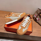 Hermes unisex sneakers on orange box, tan suede and white mesh with white laces.