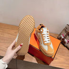 Hermes unisex sneaker with tan outsole and white laces, on orange box.