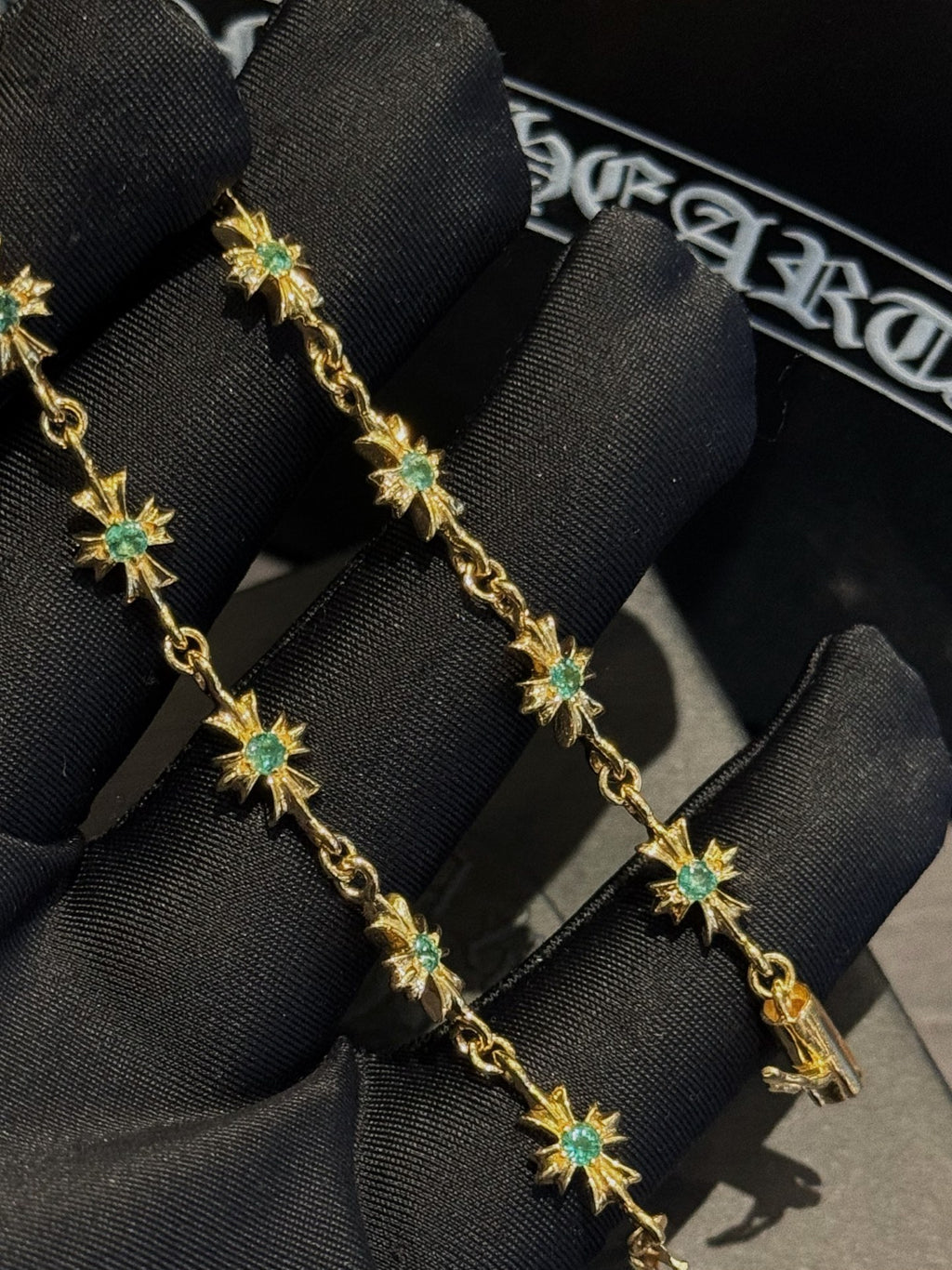 Gold bracelet with green star charms on black fabric display