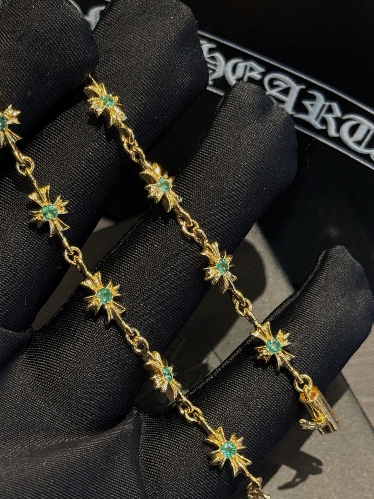 Gold bracelet with green star charms on black fabric display