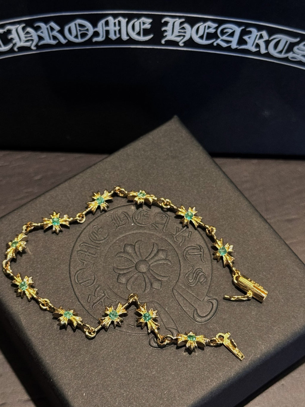 Gold bracelet with green star/flower charms and linked settings on display card