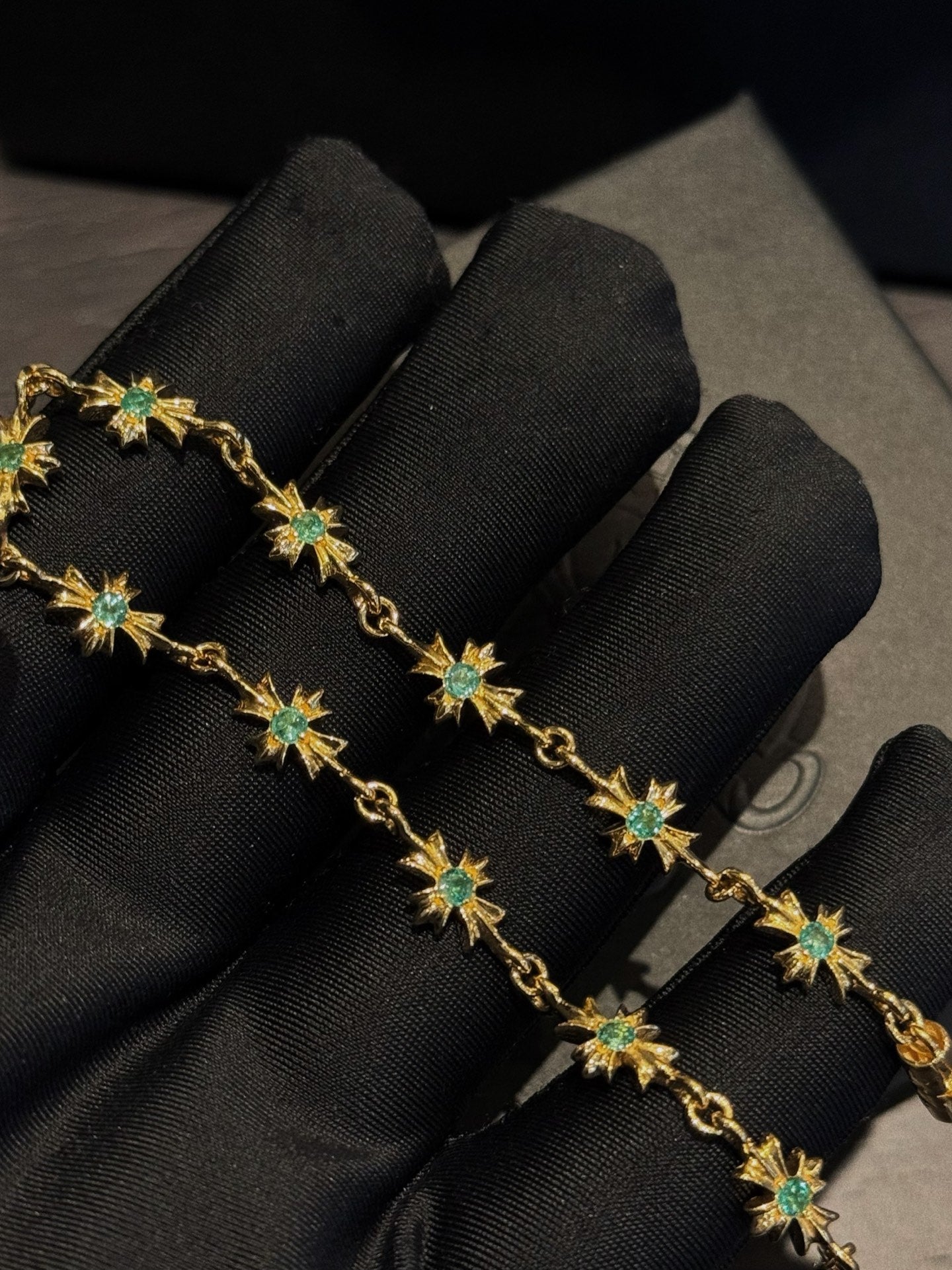 Gold bracelet with green star gemstones, coiled on black fabric display