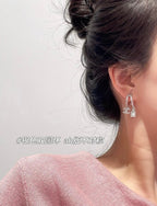 Hoop earrings with dangling charms, silver-tone, close-up profile on ear