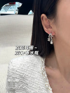 Hoop earrings with dangling charms, silver-tone, angled close-up on ear