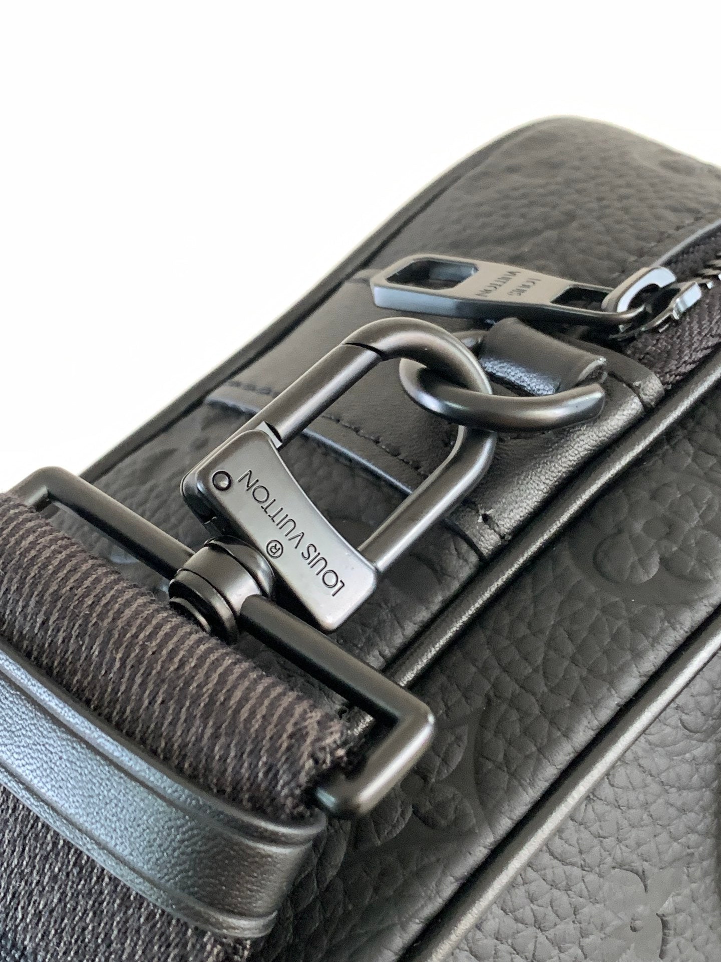 Louis Vuitton monogram bag detail: dark leather strap with metal buckle and engraved plaque