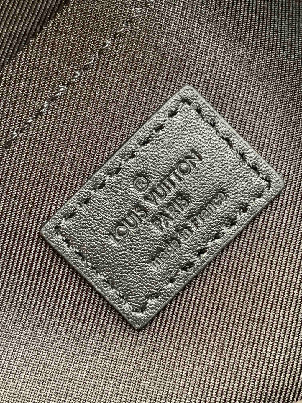 Louis Vuitton stitched label patch with embossed text and corner stitching on fabric