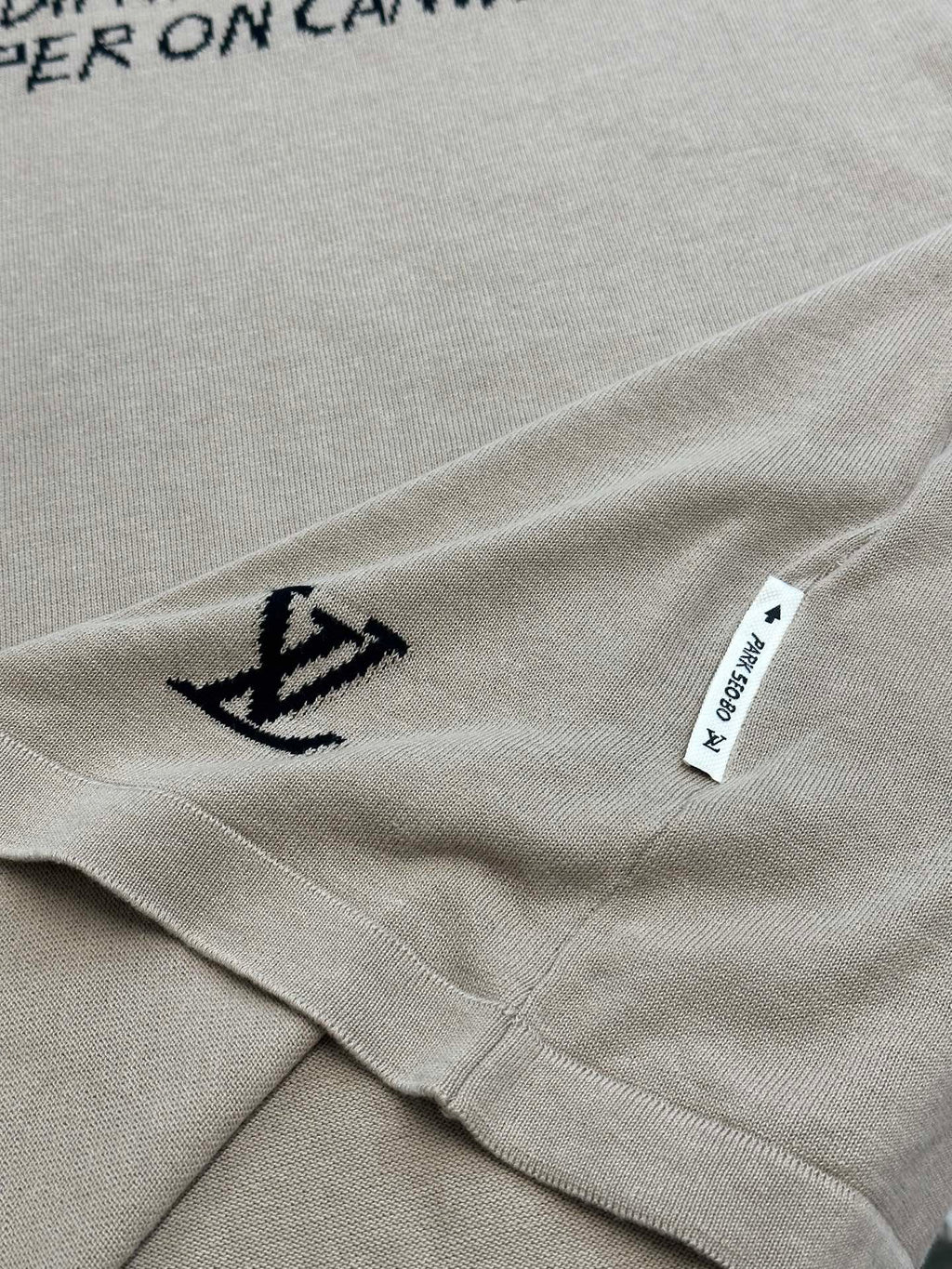 Light beige T-shirt hem detail with small black anchor icon and white care label