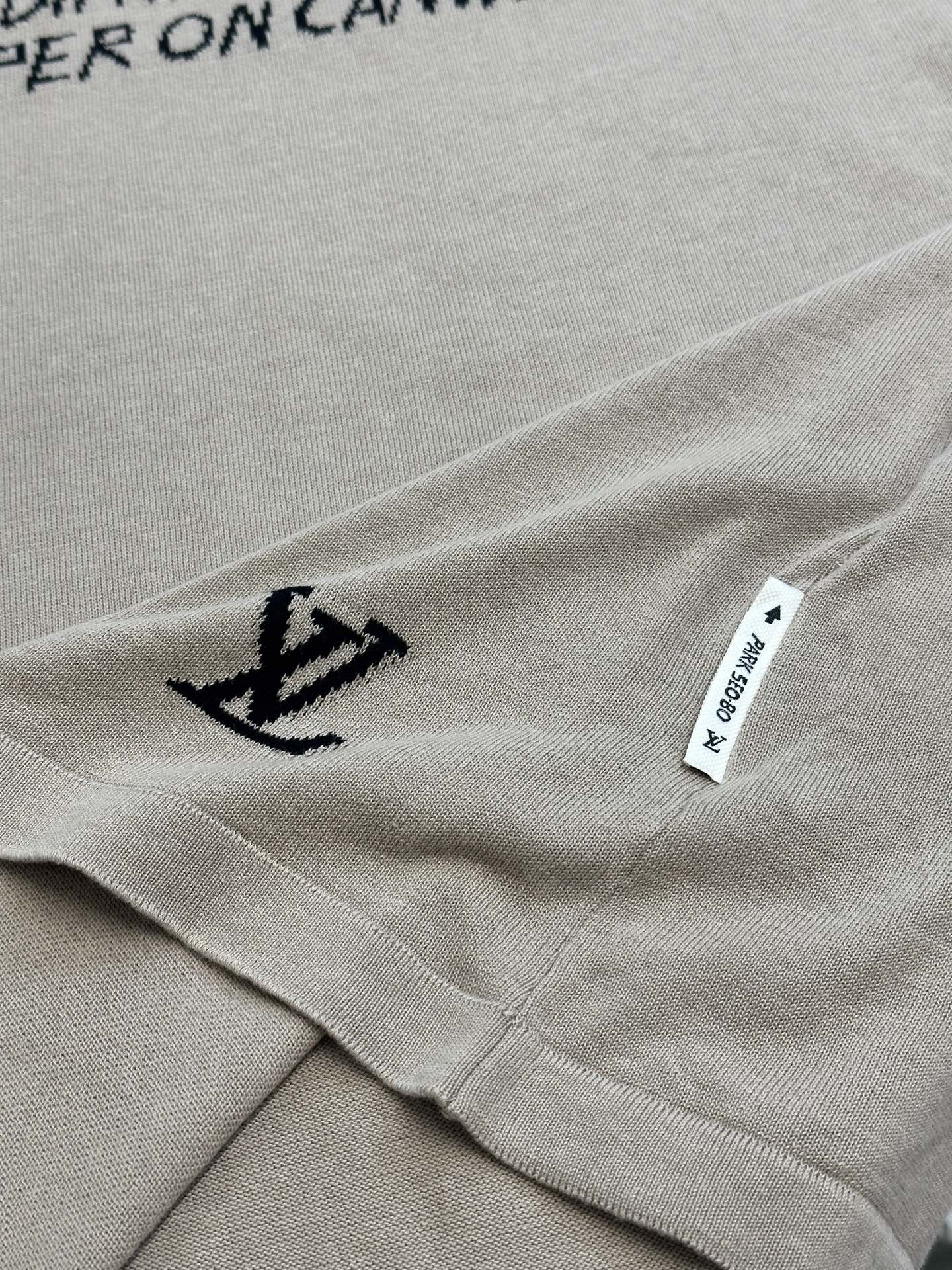 Light beige T-shirt hem detail with small black anchor icon and white care label