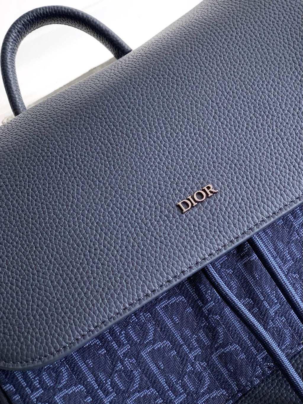 Dior bag close-up of textured gray flap and blue monogram side panel with stitching