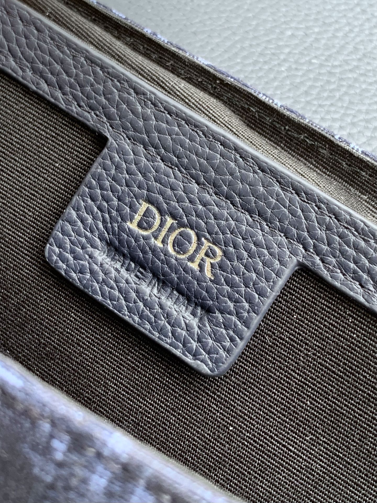 Navy Dior bag close-up of embossed “DIOR” logo on pebbled leather panel.