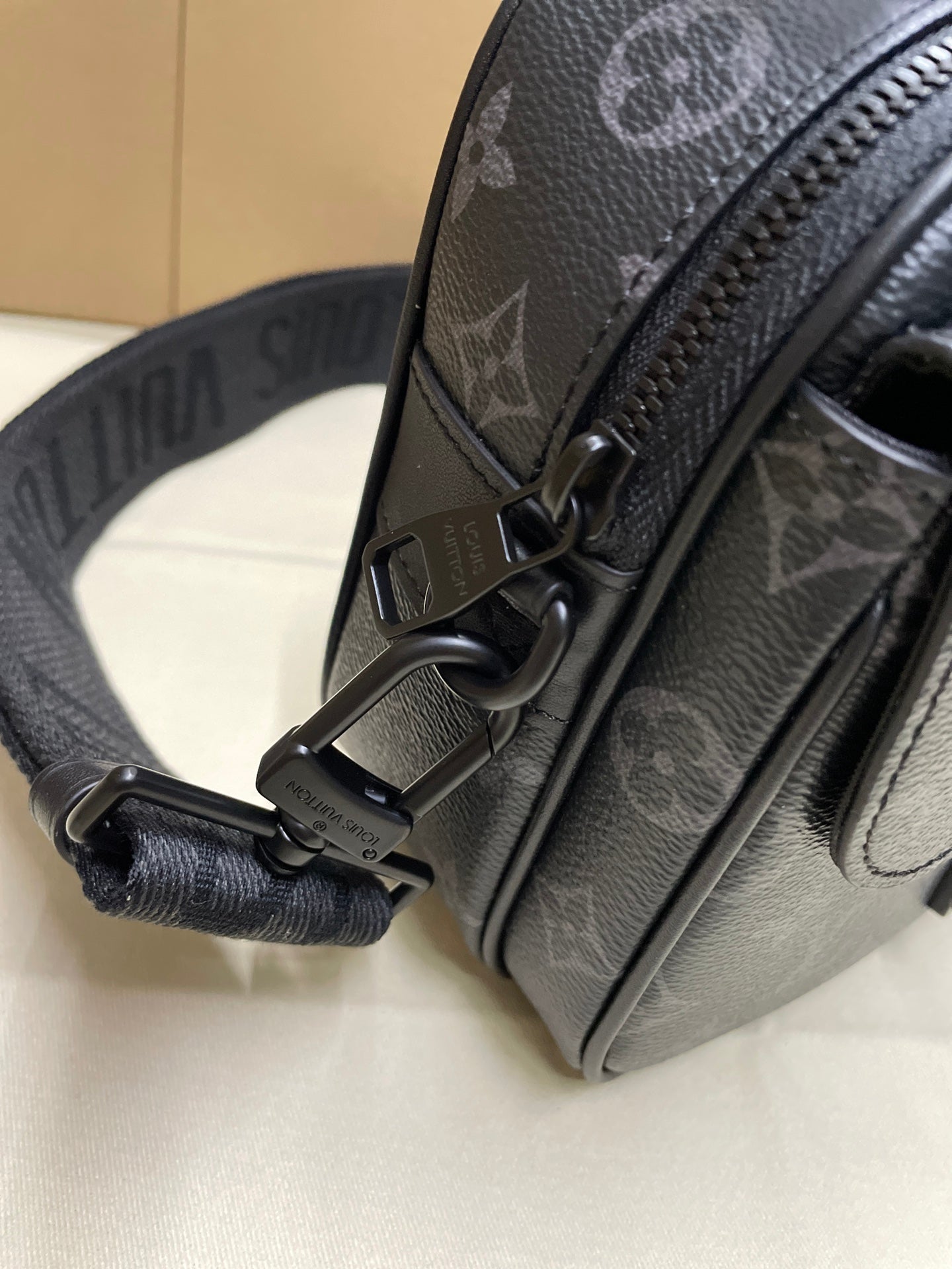 Dark monogram crossbody bag strap with metal hardware, close-up
