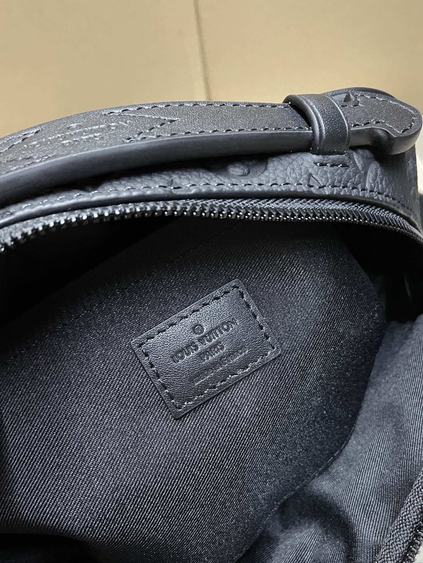 Louis Vuitton men's bag close-up of stitched logo patch and zipper trim on dark fabric