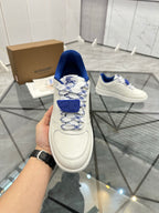 White low-top sneaker close-up with blue collar, patterned laces, and strap detail