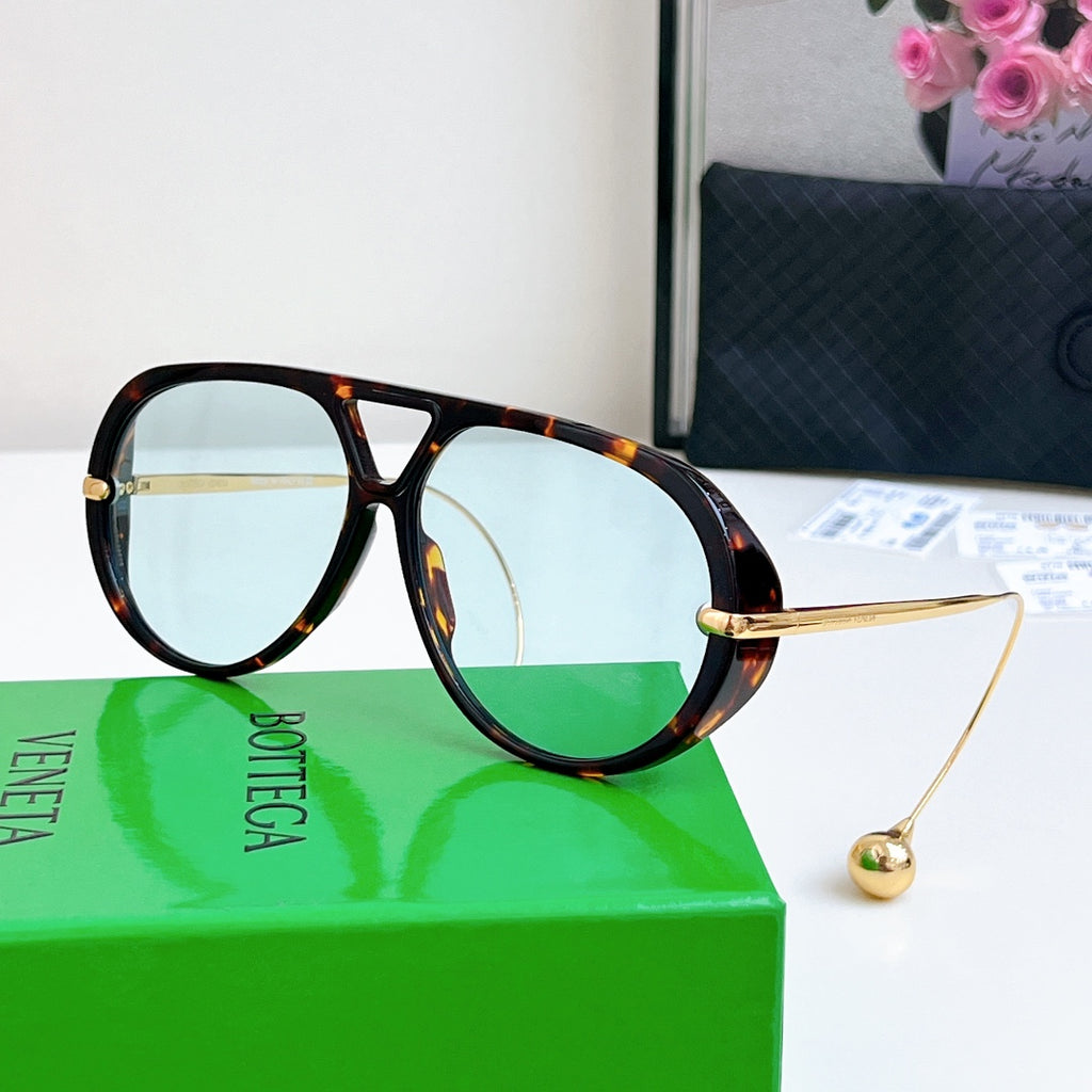 Sunglasses with tortoiseshell frame, gold accents, and green-tinted lenses.