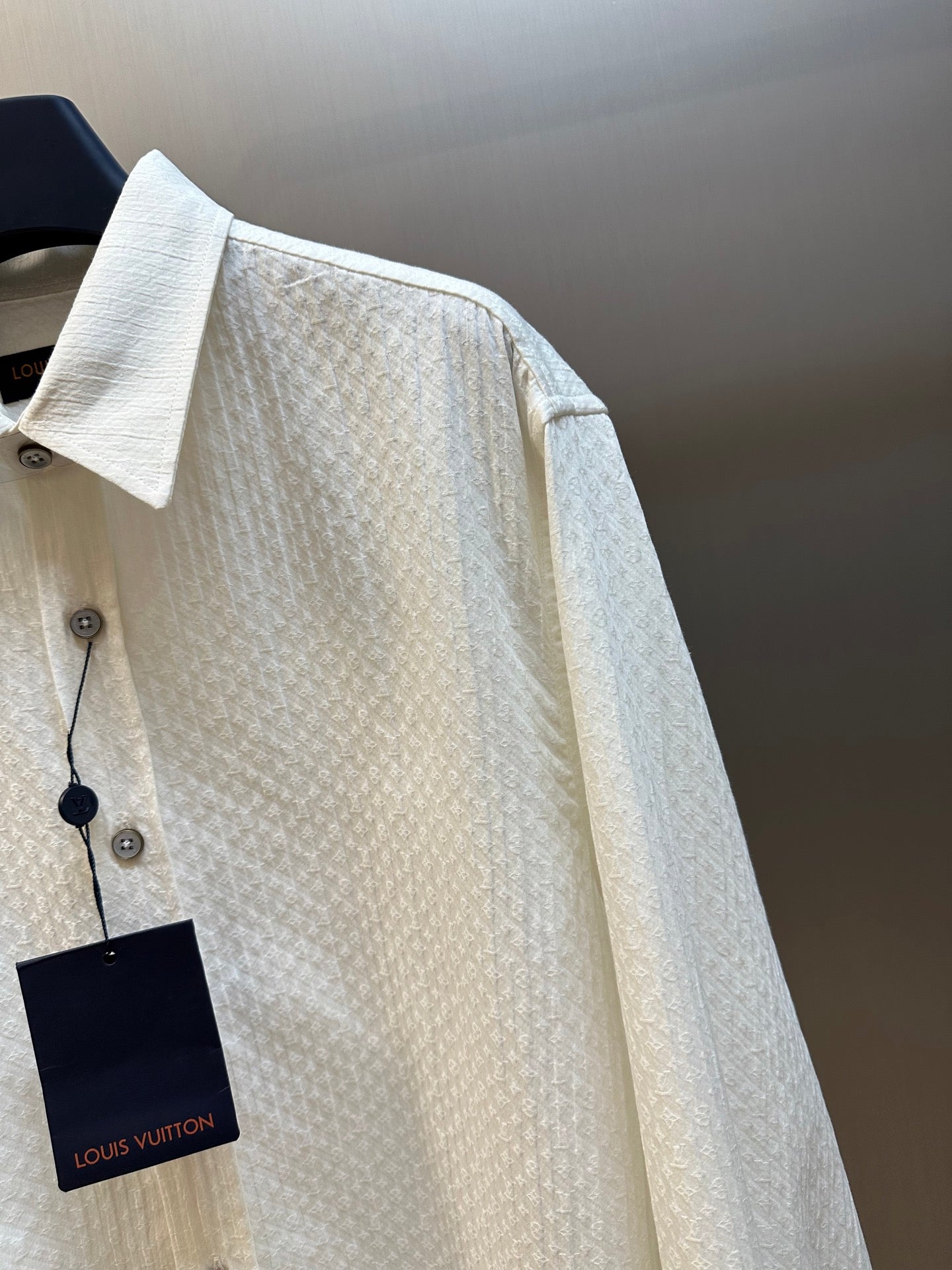 Cream textured long-sleeve shirt with buttoned chest, spread collar, and side tag