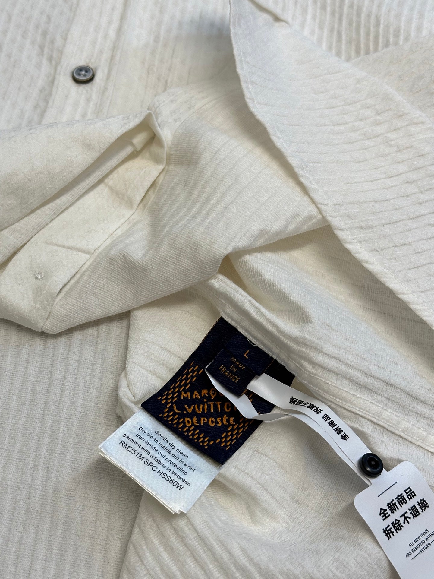 Cream long-sleeve shirt with collar, buttons, and inner label tags on placket