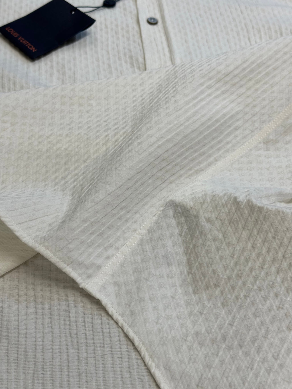 Cream textured shirt fabric close-up with top tag and collar button area