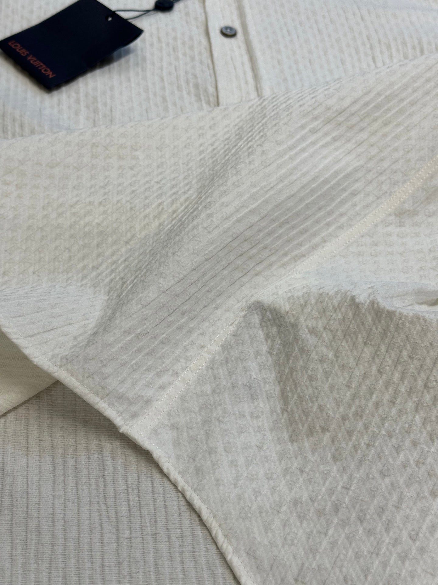Cream textured shirt fabric close-up with top tag and collar button area