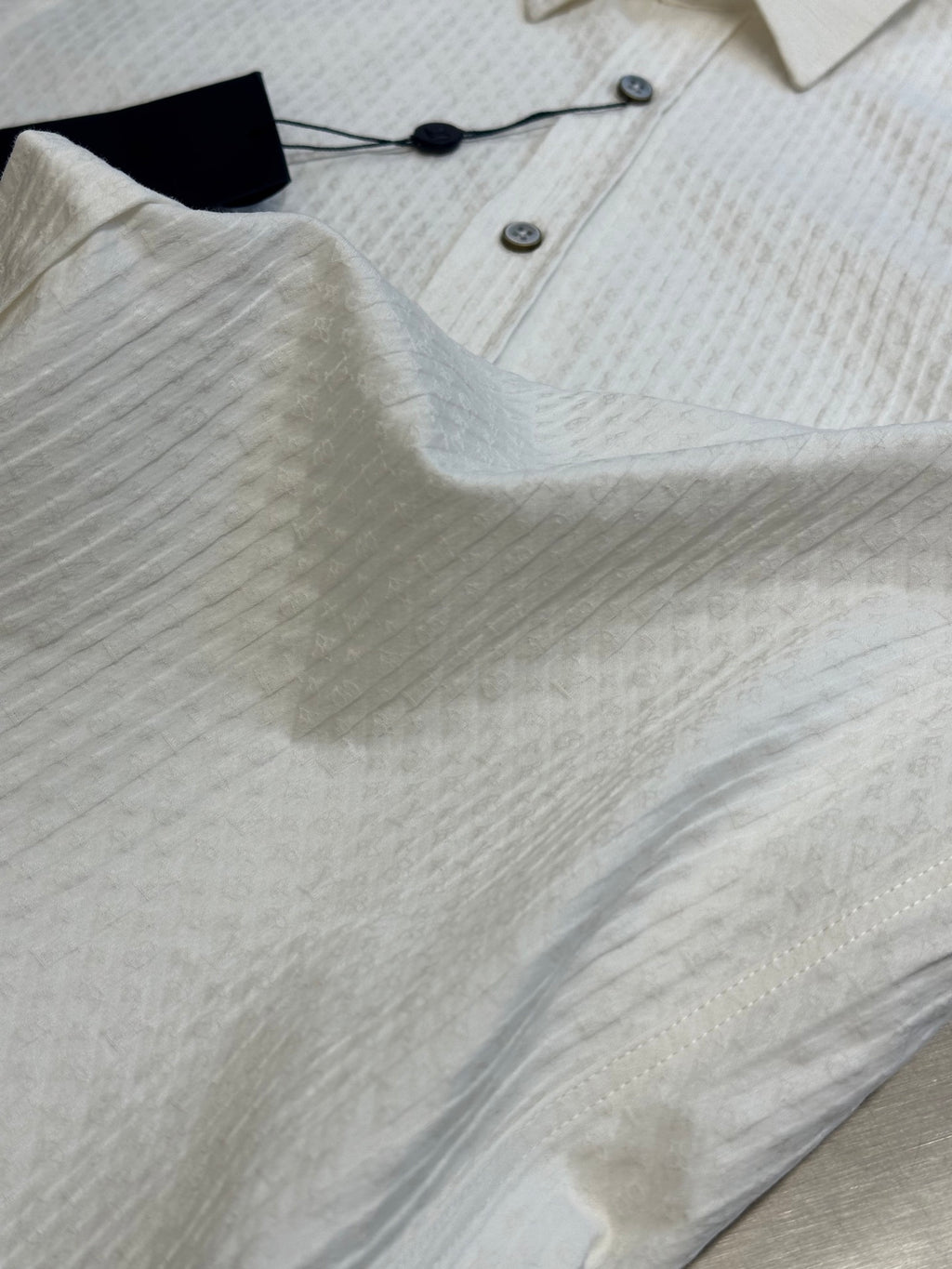 Cream textured short-sleeve style? Actually long-sleeve polo? V-neck? Close-up of cream shirt hem